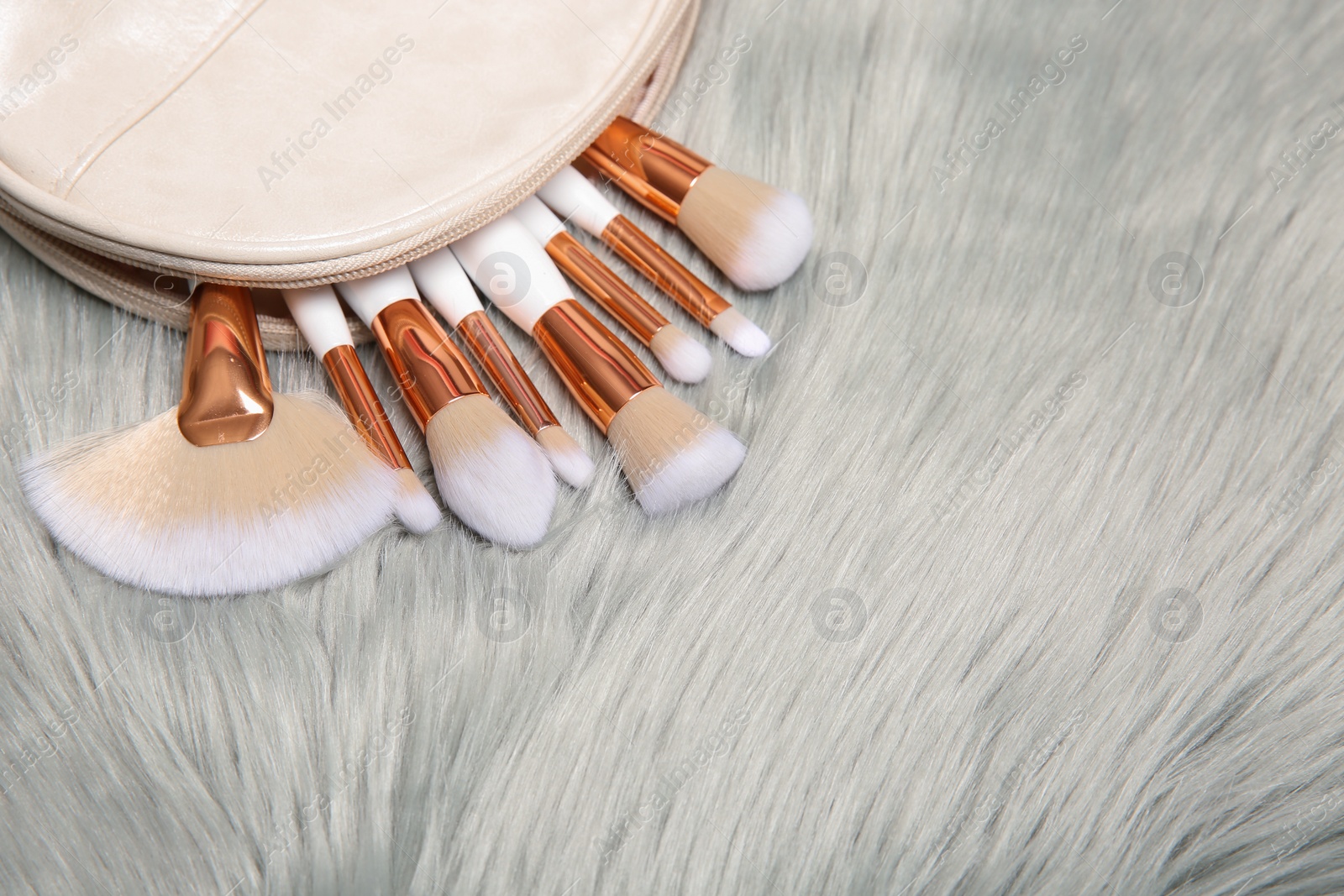 Photo of Bag with set of professional makeup brushes on furry fabric. Space for text