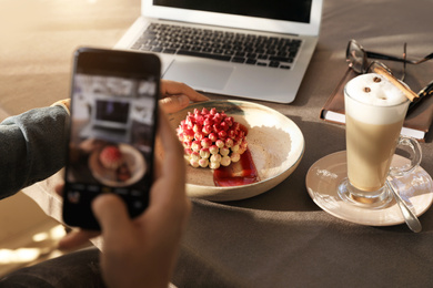 Photo of Young blogger taking picture of dessert at table in cafe, closeup
