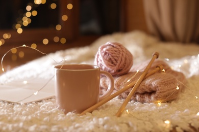 Composition with cup of hot beverage, knitting yarn and book on fuzzy rug. Winter evening