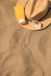 Photo of Sunscreen, straw hat and flower on sandy beach, top view and space for text. Sun protection