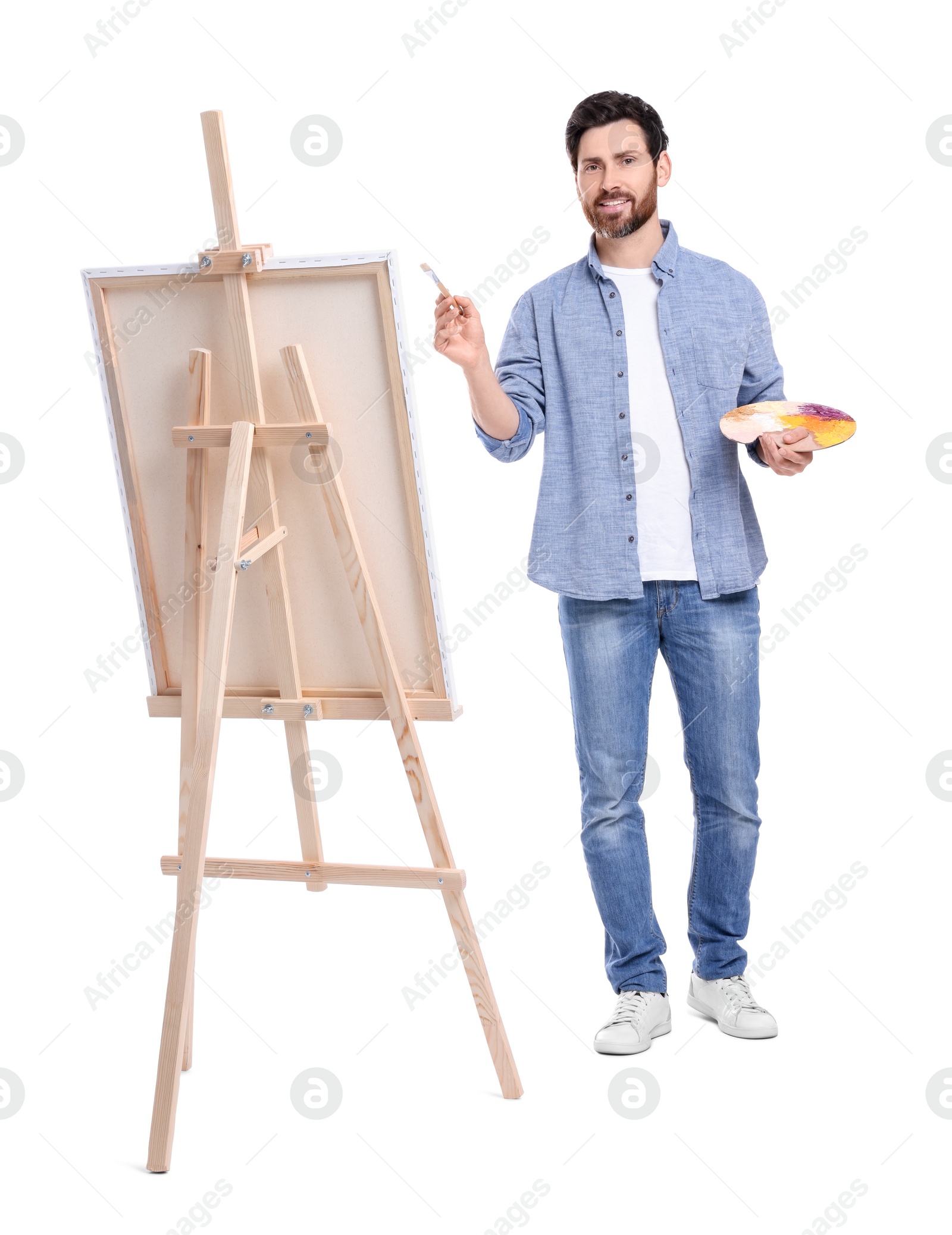 Photo of Happy man painting with brush against white background. Using easel to hold canvas