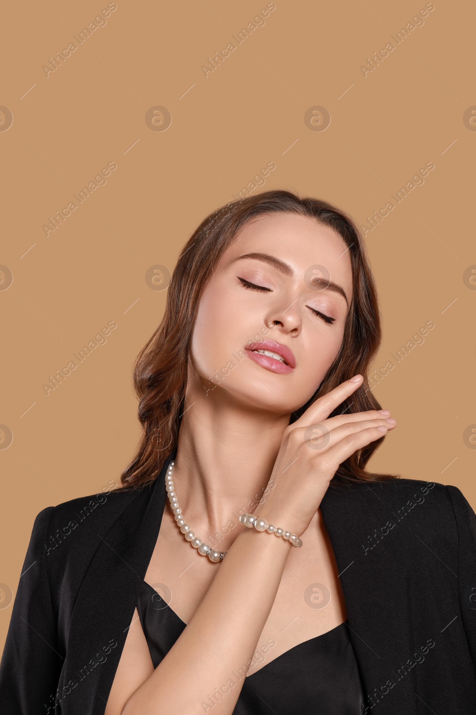 Photo of Young woman wearing elegant pearl jewelry on brown background