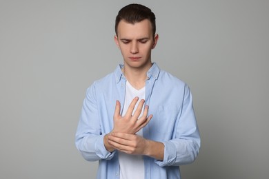 Photo of Young man suffering from pain in his hand on light grey background. Arthritis symptoms