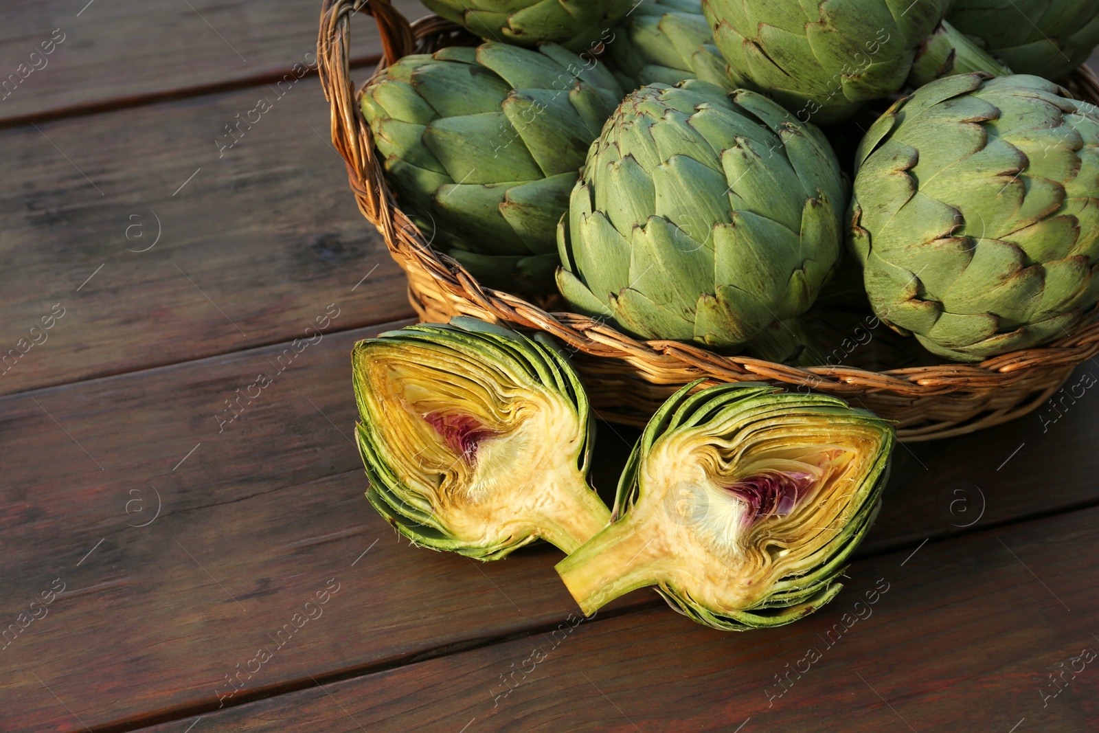 Photo of Wicker basket with fresh raw artichokes on wooden table