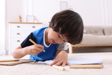 Photo of Cute little boy drawing with pencils on floor at home