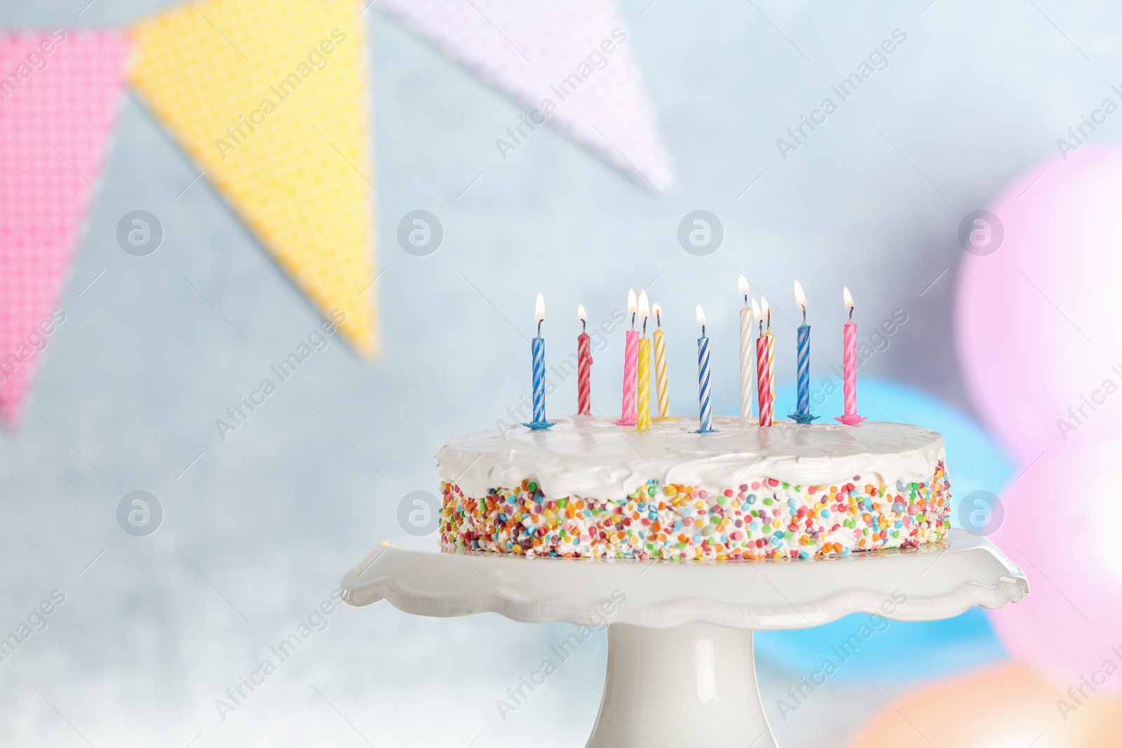 Photo of Tasty birthday cake with burning candles on stand against blurred background, space for text