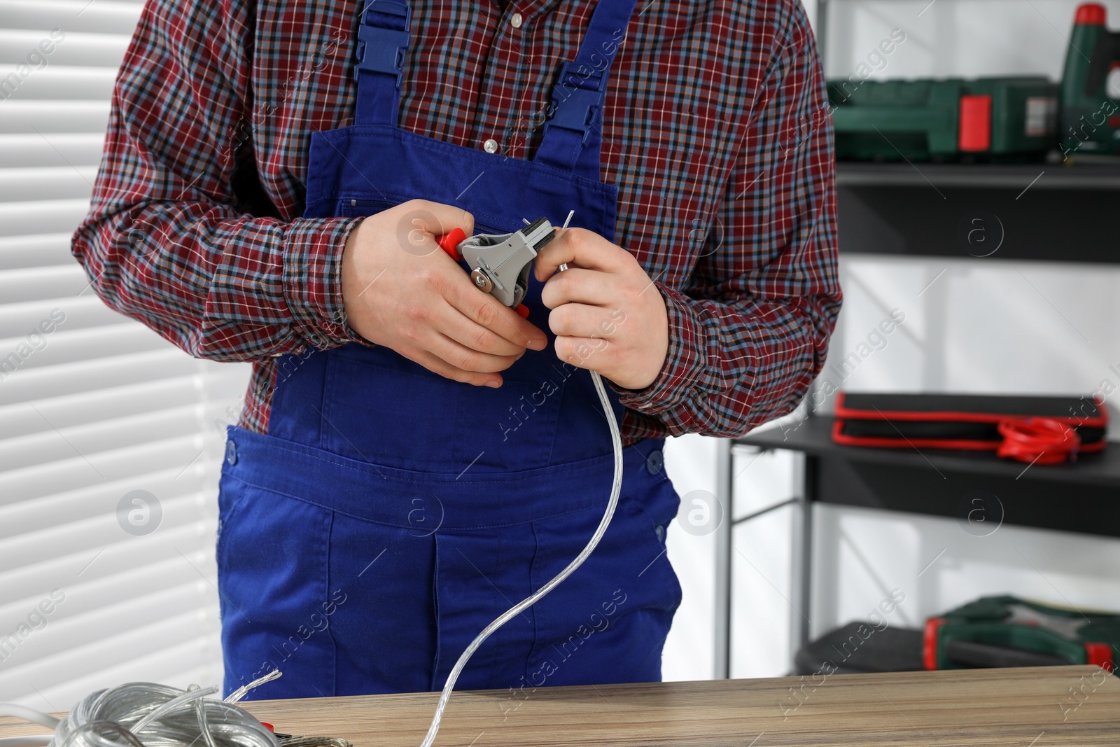 Photo of Professional electrician in uniform stripping wiring indoors, closeup