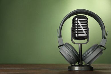 Photo of Microphone and modern headphones on wooden table against green background, space for text