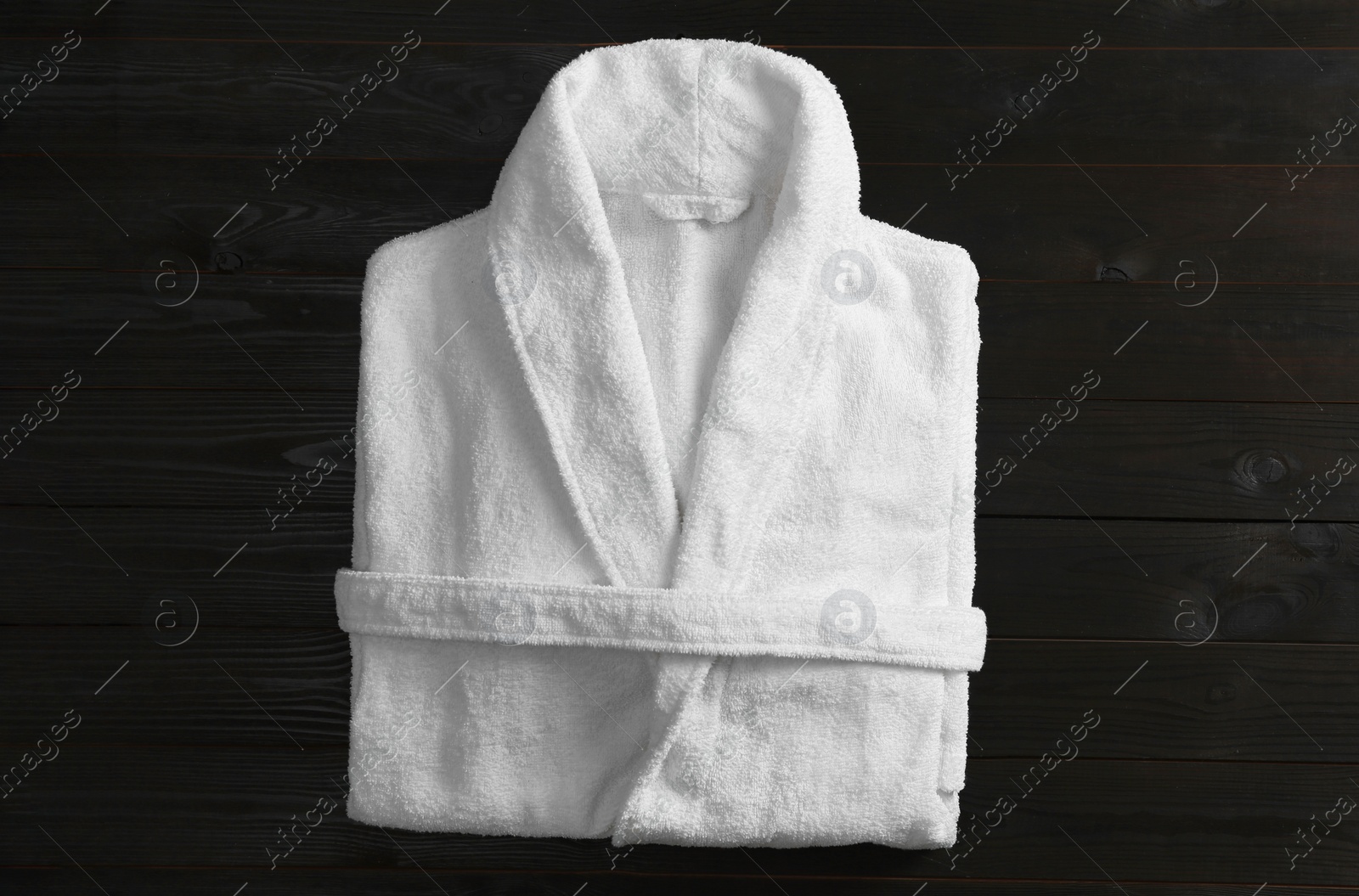 Photo of Clean folded bathrobe on black wooden background, top view