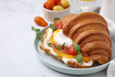 Photo of Tasty croissant with fried egg, tomato and microgreens on white table, closeup. Space for text