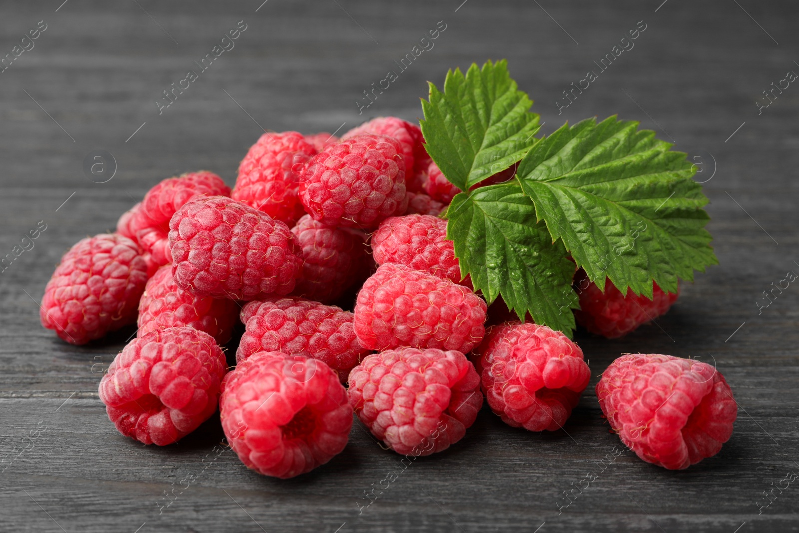 Photo of Delicious fresh ripe raspberries with leaves on dark wooden table