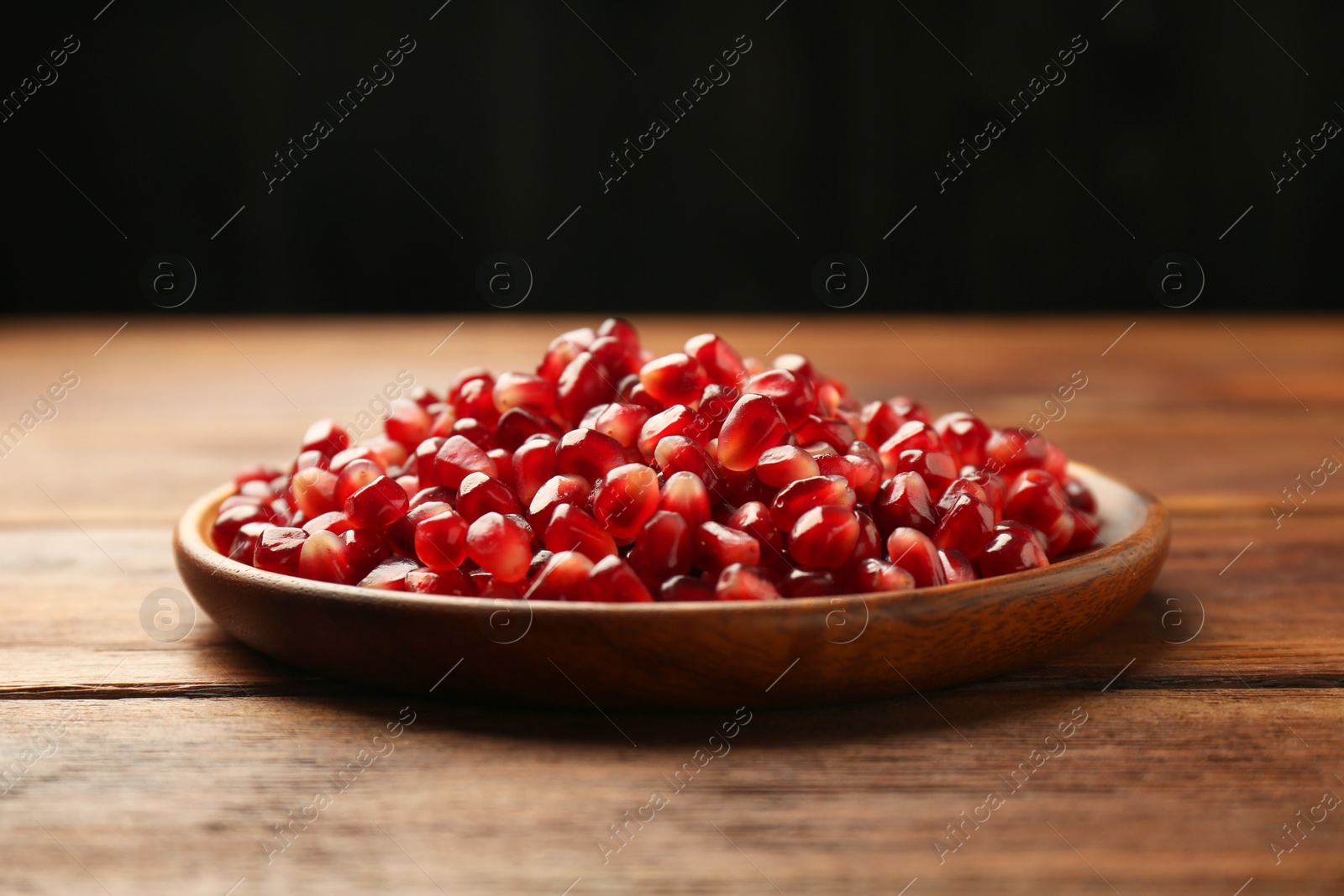 Photo of Tasty ripe pomegranate grains on wooden table