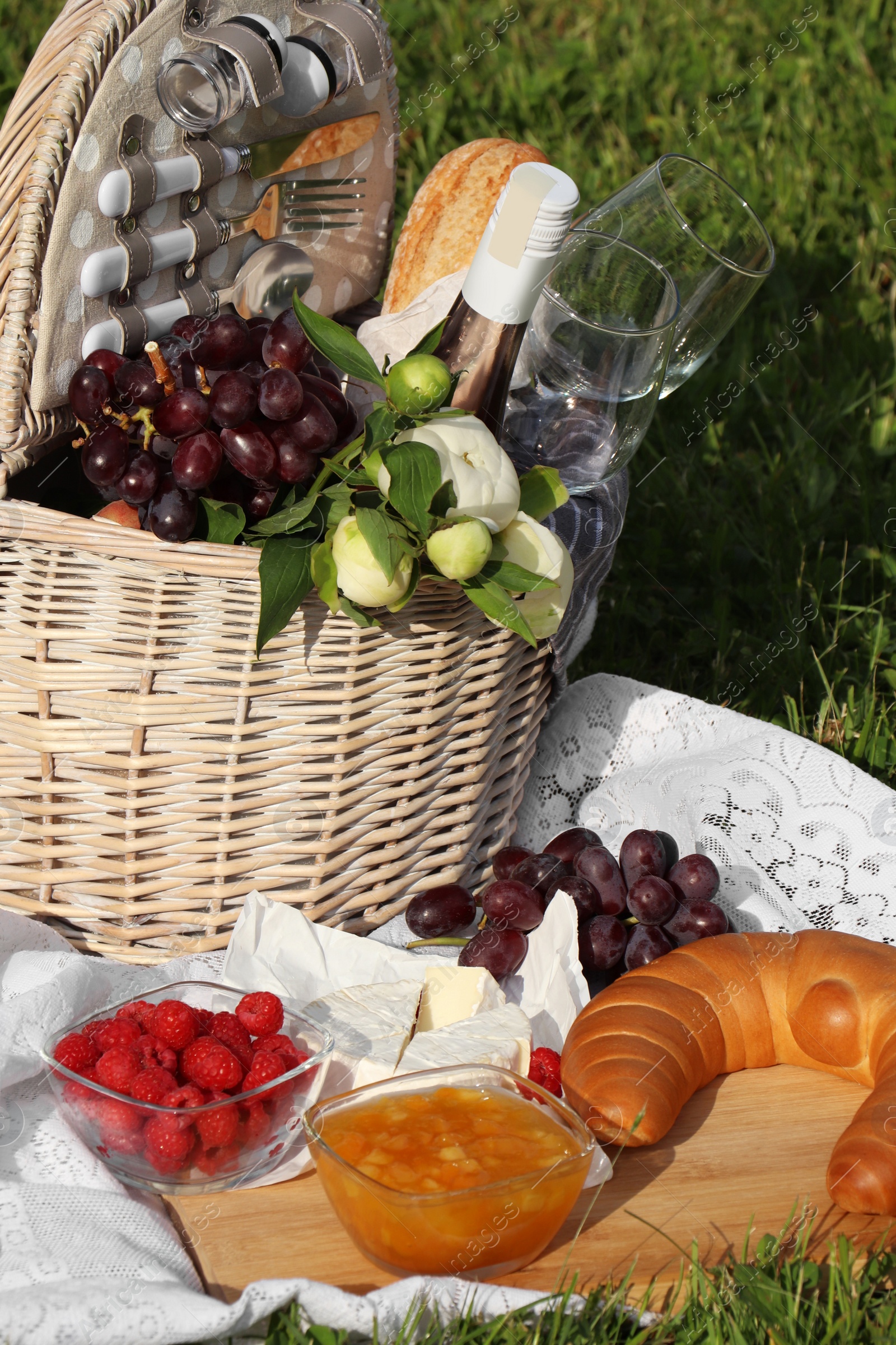 Photo of Picnic blanket with tasty food, flowers, basket and cider on green grass outdoors