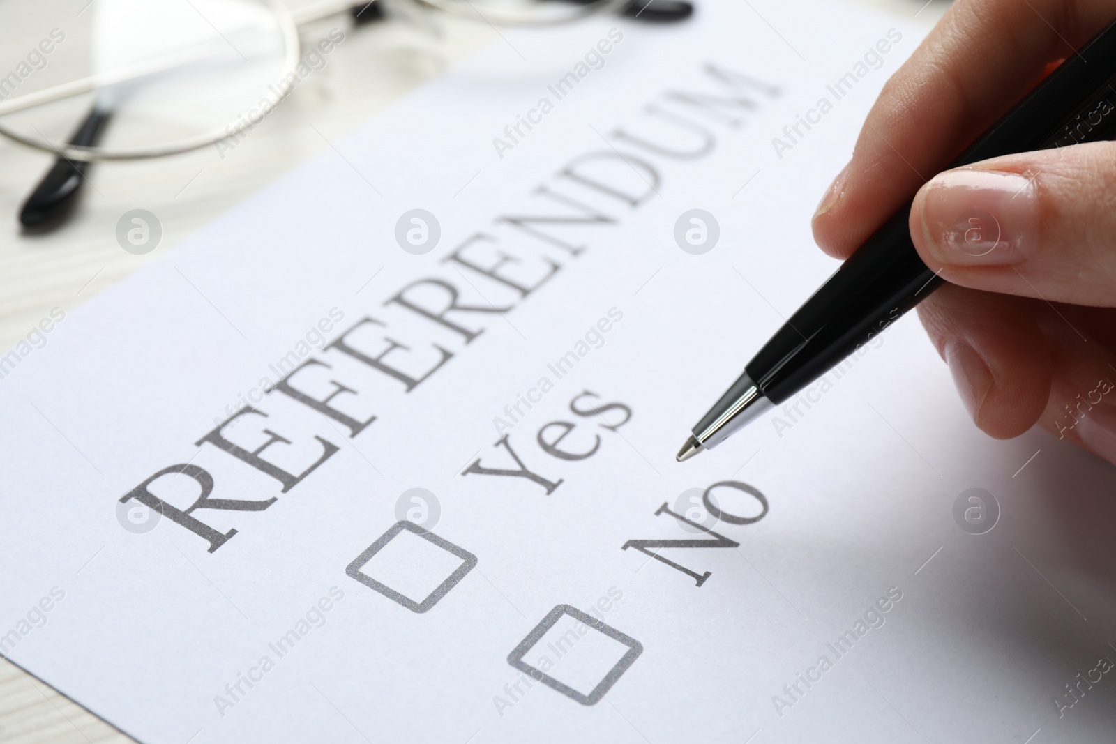 Photo of Woman with referendum ballot making decision at white table, closeup