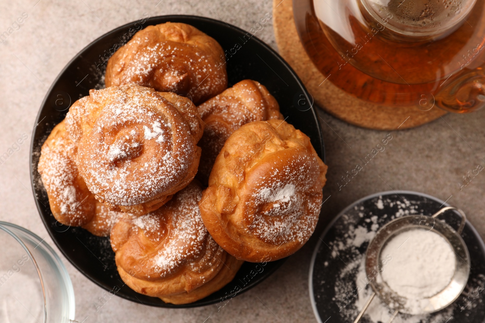 Photo of Delicious profiteroles with powdered sugar and tea on grey table, flat lay