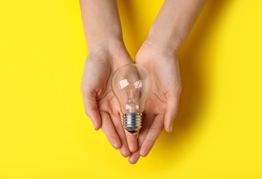 Photo of Woman holding light bulb on yellow background, top view