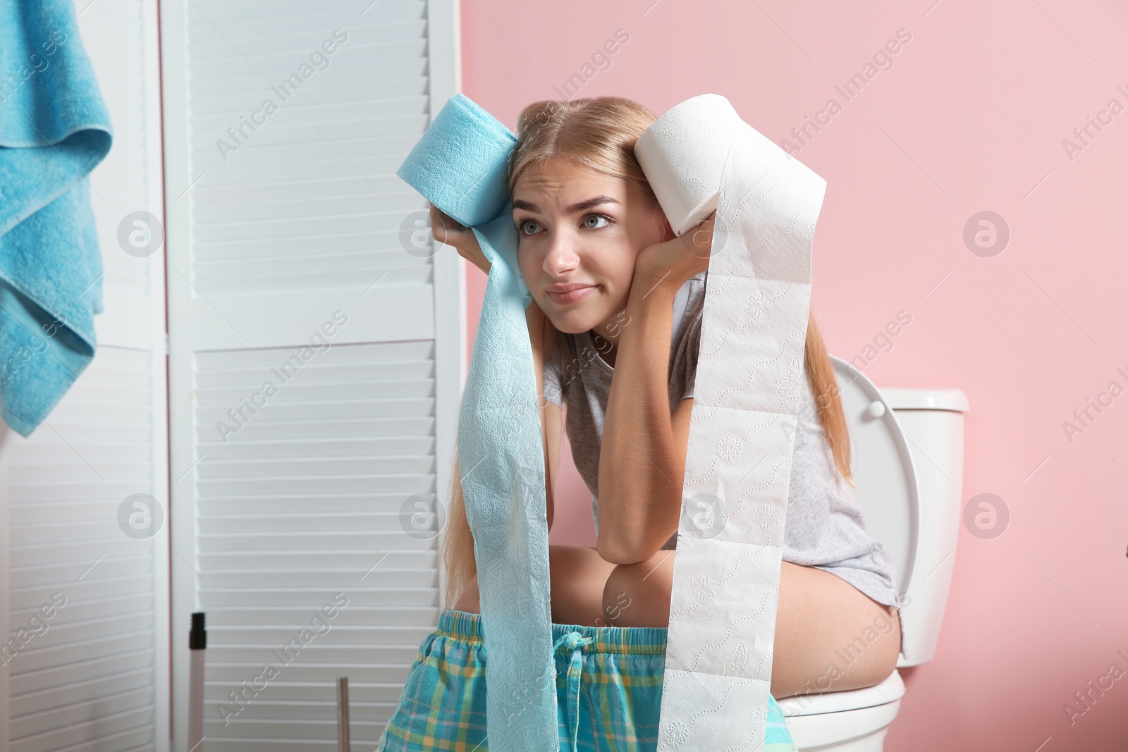 Photo of Woman with paper rolls sitting on toilet bowl in bathroom