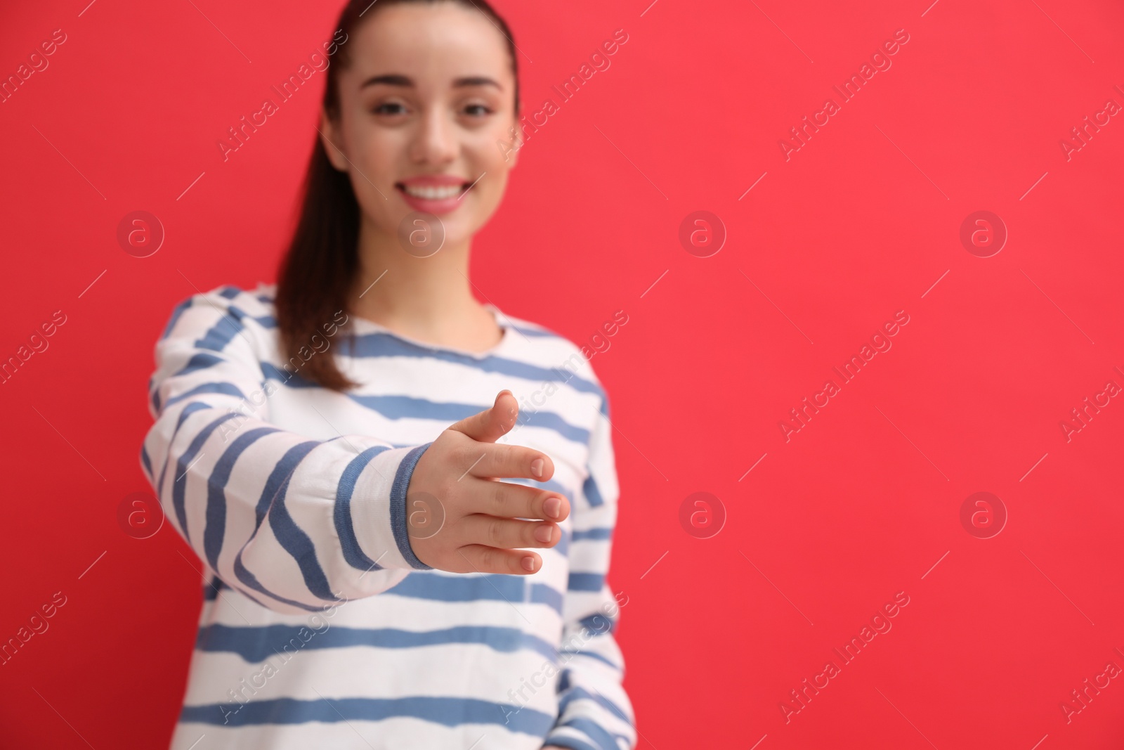 Photo of Happy young woman offering handshake against red background, focus on hand. Space for text