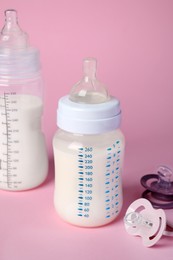 Photo of Feeding bottles with milk and baby pacifiers on pink background