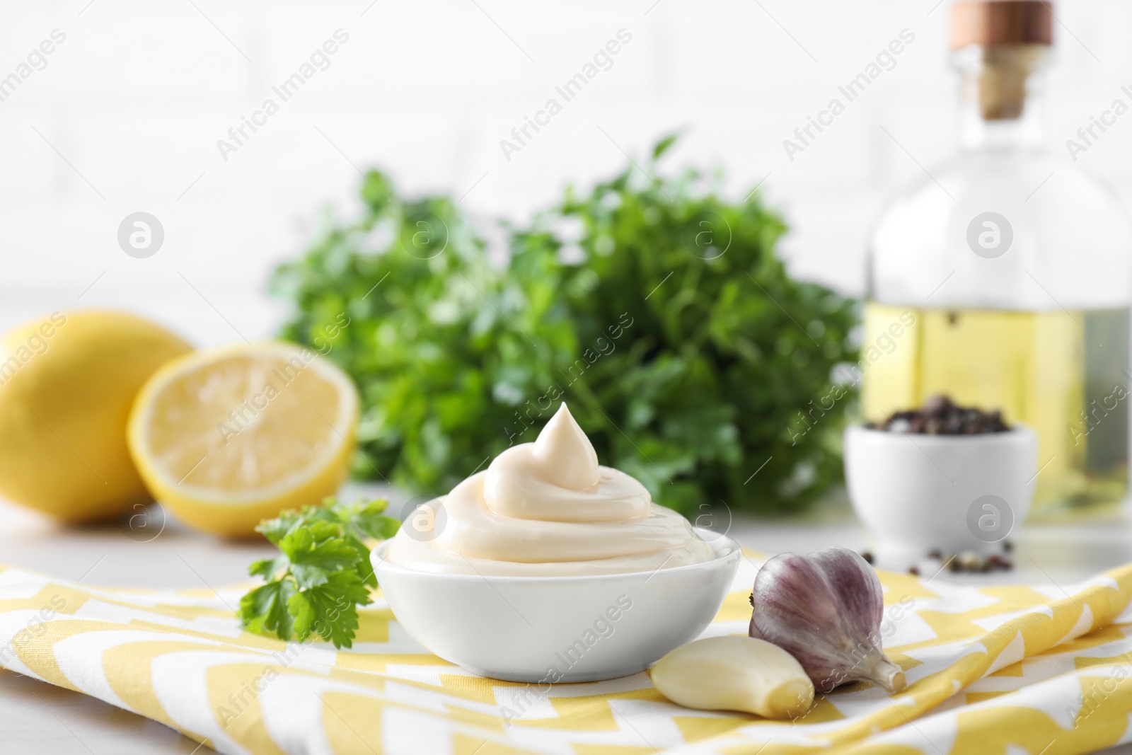 Photo of Tasty mayonnaise sauce in bowl, parsley and garlic on table