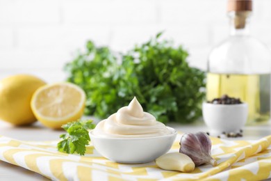 Tasty mayonnaise sauce in bowl, parsley and garlic on table