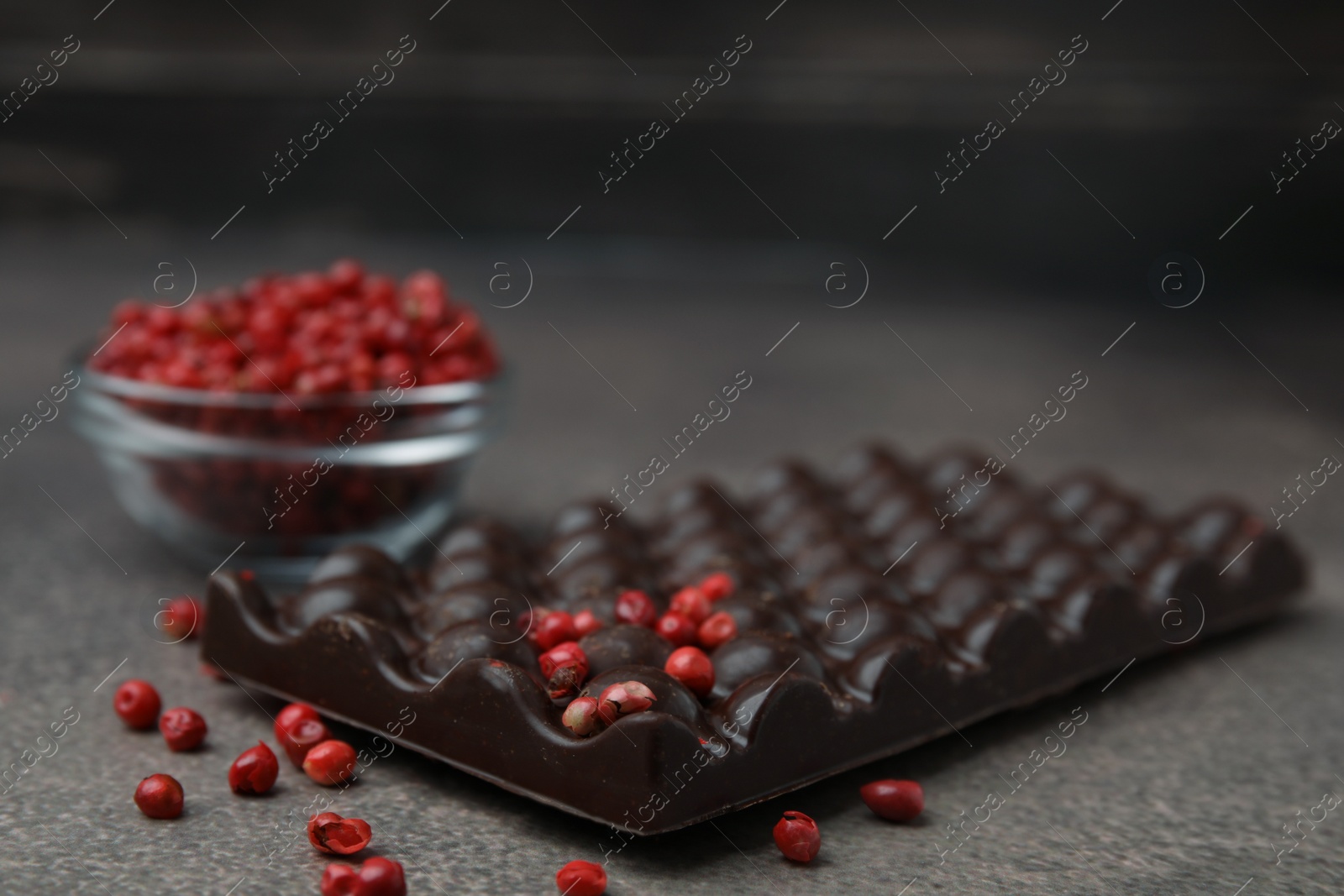 Photo of Delicious chocolate bar and red peppercorns on grey textured table, closeup