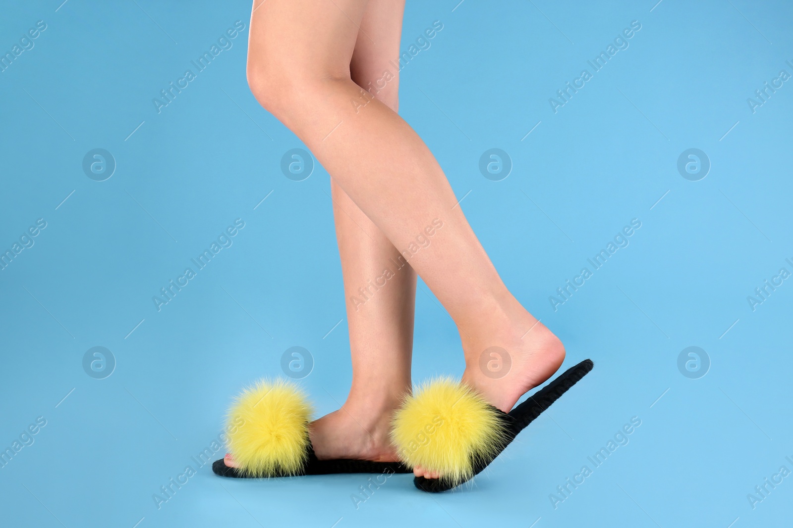 Photo of Woman in fluffy slippers on light blue background, closeup