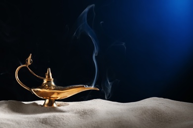 Photo of Aladdin magic lamp on sand against dark background