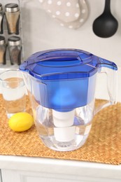 Photo of Water filter jug, glass and lemon on countertop in kitchen