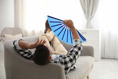 Photo of Man with hand fan lying on sofa. Summer season