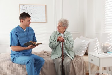 Photo of Caregiver reading book to senior woman indoors. Home health care service