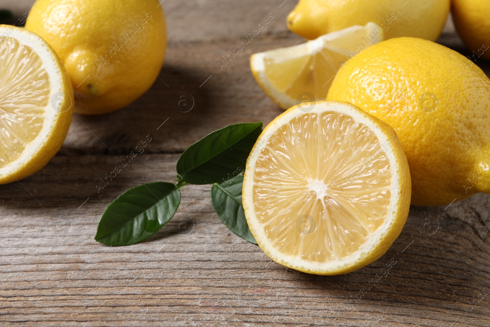 Photo of Fresh lemons and green leaves on wooden table, closeup