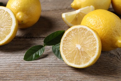 Fresh lemons and green leaves on wooden table, closeup