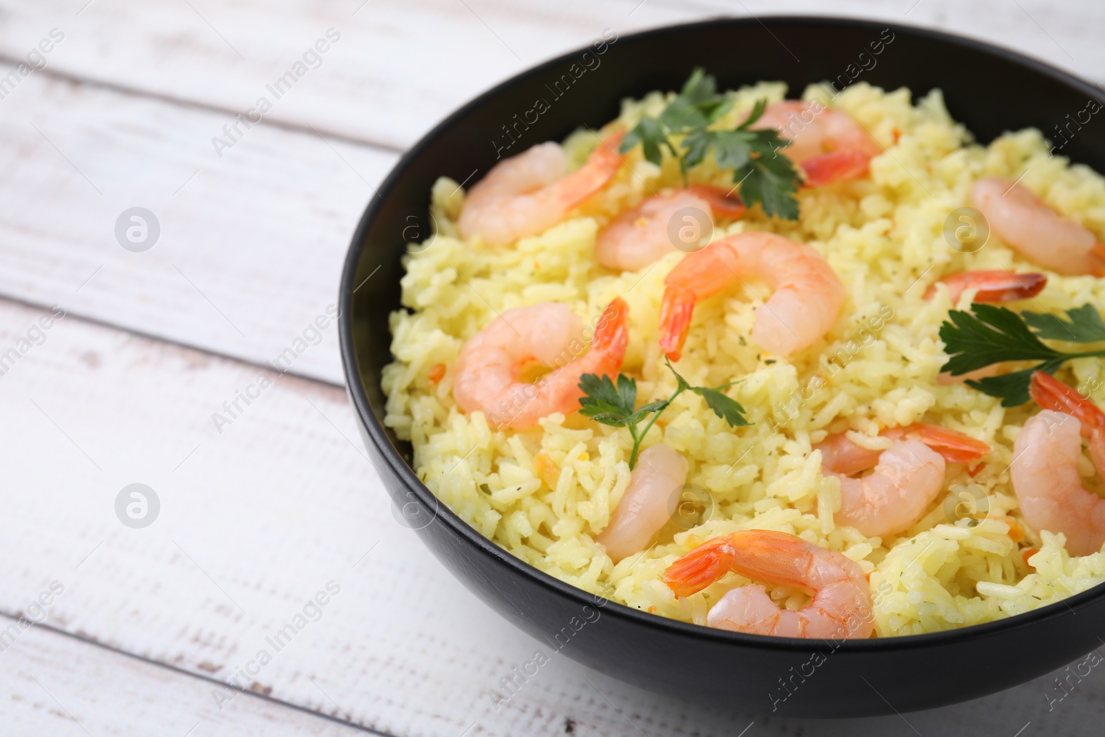 Photo of Delicious risotto with shrimps and parsley in bowl on white wooden table, closeup. Space for text