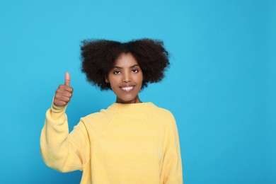 Photo of Happy African American woman showing thumbs up on light blue background. Space for text