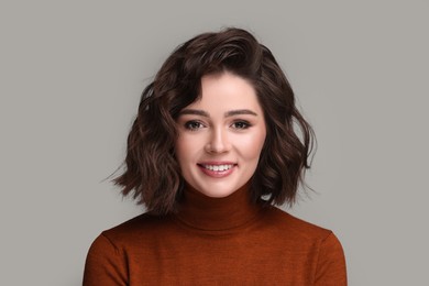 Portrait of beautiful young woman with wavy hairstyle on grey background