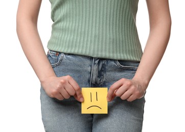 Cystitis. Woman holding sticky note with drawn sad face on white background, closeup