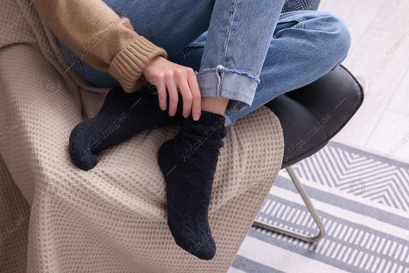 Photo of Woman in warm socks sitting on armchair at home, closeup