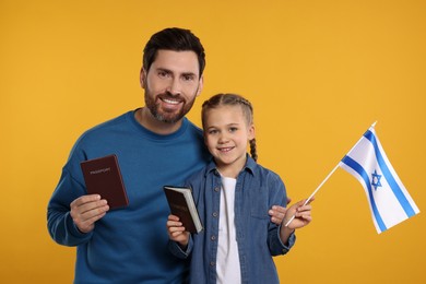 Photo of Immigration. Happy man with his daughter holding passports and flag of Israel on orange background