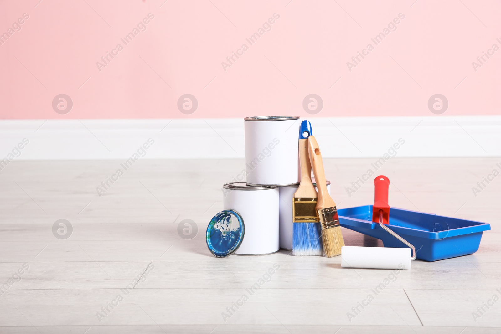 Photo of Cans of paint and decorator tools on wooden floor indoors. Space for text