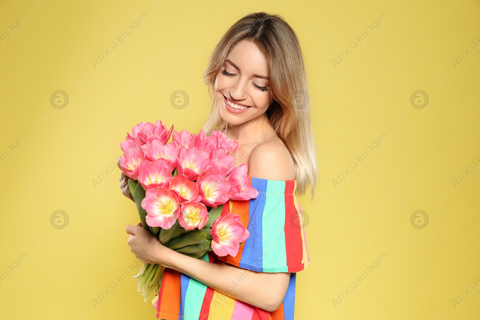 Photo of Portrait of beautiful smiling girl with spring tulips on yellow background. International Women's Day