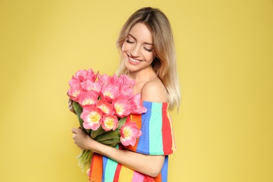 Portrait of beautiful smiling girl with spring tulips on yellow background. International Women's Day