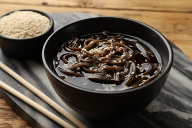 Tasty soup with buckwheat noodles (soba), sesame and chopsticks on table, closeup