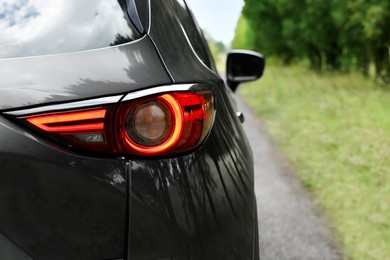 New black modern car on road near trees, closeup of taillight