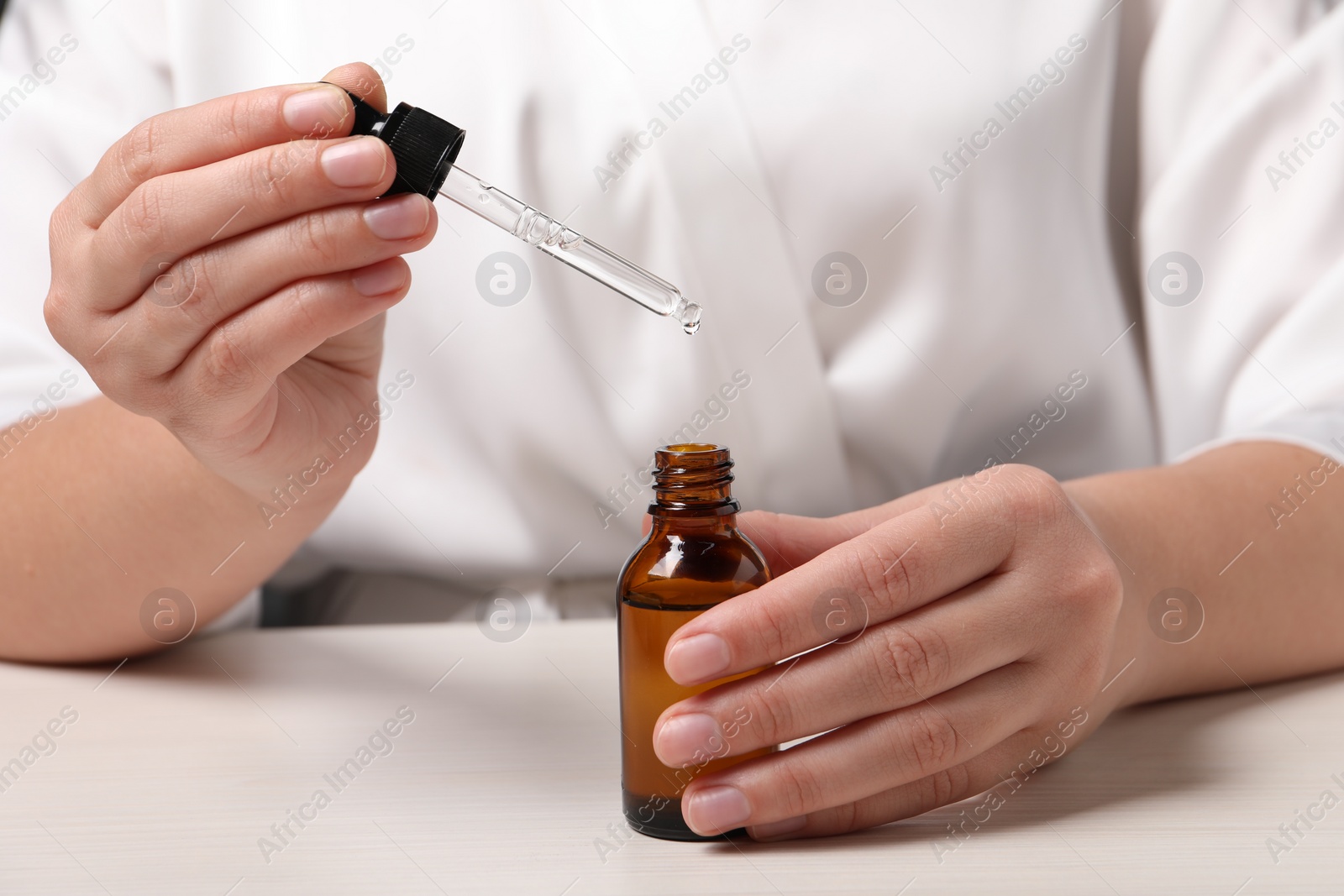 Photo of Woman with bottle of cosmetic serum and pipette at white table, closeup