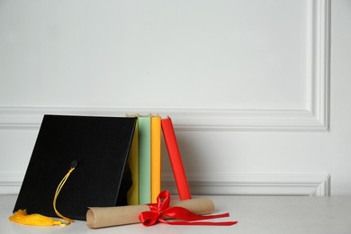 Photo of Graduation hat, books and diploma on floor near white wall, space for text