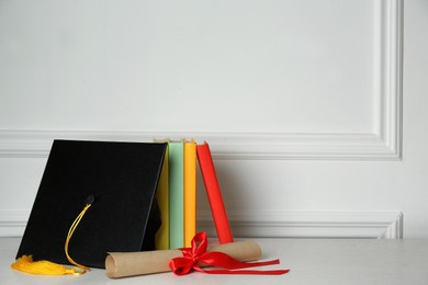 Graduation hat, books and diploma on floor near white wall, space for text