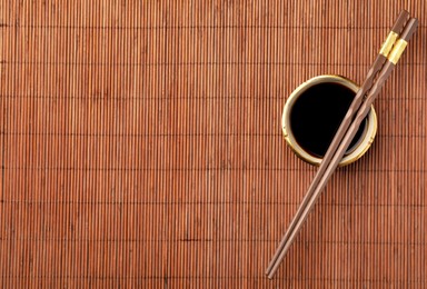 Bowl of soy sauce and chopsticks on bamboo mat, flat lay. Space for text