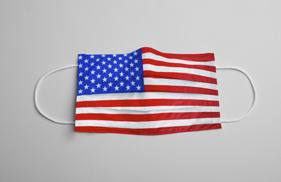 Image of Medical protective mask with USA flag pattern on light grey background, top view. Dangerous virus