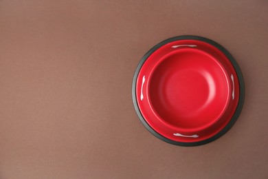 Empty red feeding bowl on brown background, top view. Space for text